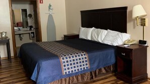 Une chambre d’hôtel avec un grand lit, un plancher en bois, une table de chevet avec une lampe et une salle de bain visible à travers une porte ouverte.