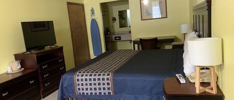 Una habitación de hotel con cama, escritorio, televisor, cómoda y lámpara.