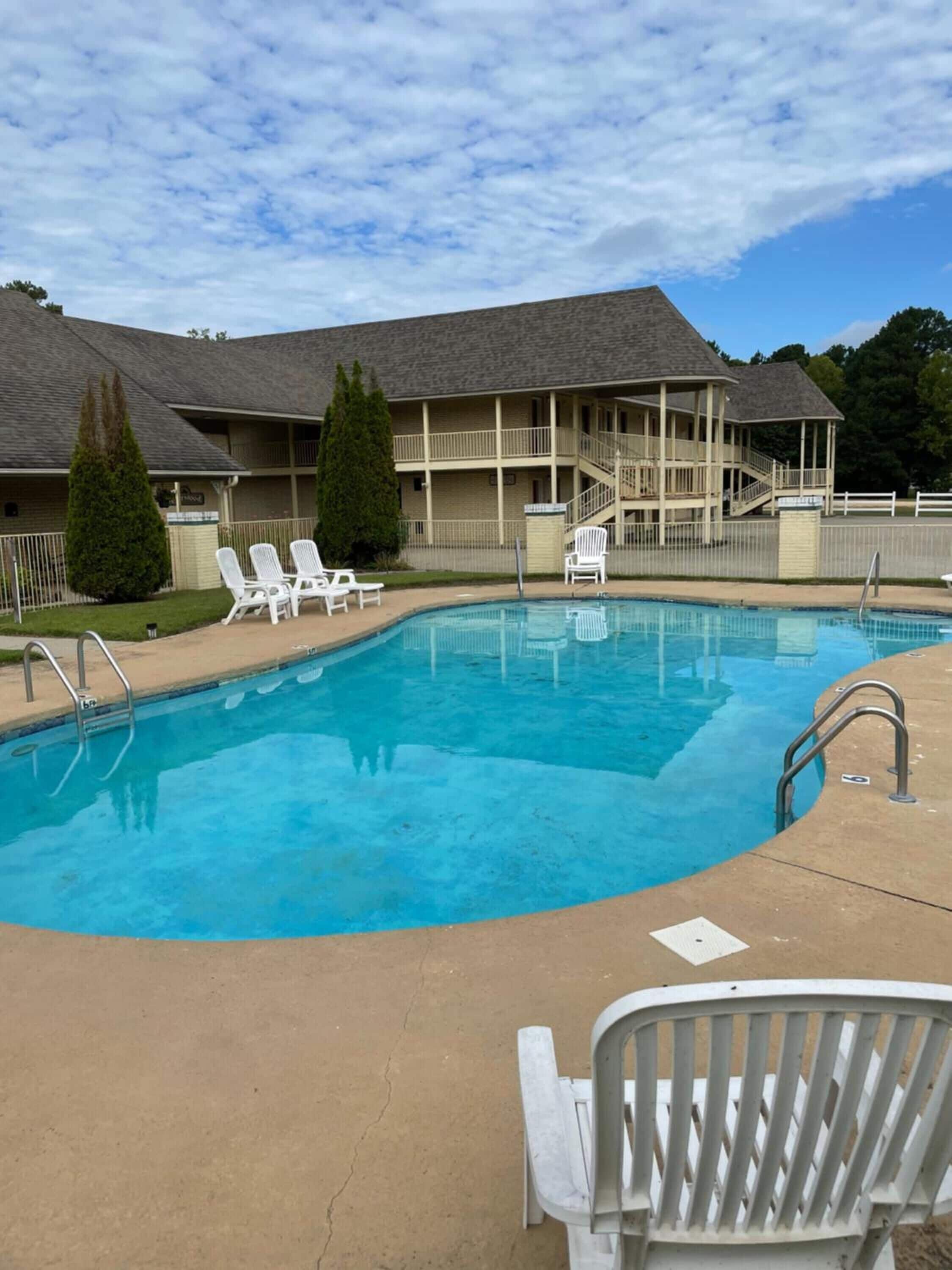 A swimming pool with lounge chairs, a covered deck, and a building with a grey roof.