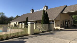 Un bâtiment à deux étages avec une façade en briques, un porche couvert et une piscine entourée d’une clôture.