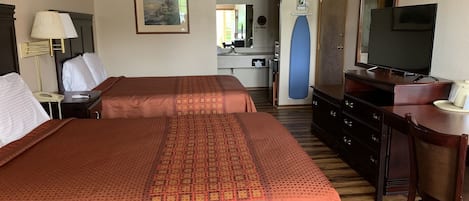 Une chambre d’hôtel avec deux lits, un bureau, une commode, une télévision et une salle de bain visible à travers une porte ouverte.