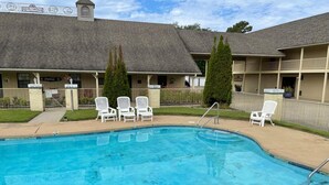 Une piscine avec des chaises longues, un espace délimité par une clôture et un bâtiment sur lequel est apposée une enseigne indiquant « Riverwood ».