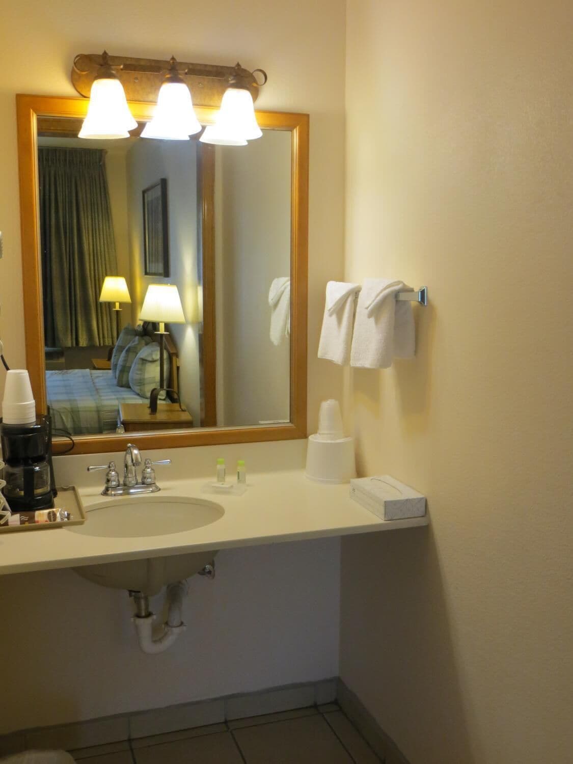 A hotel bathroom with a sink, mirror, towel rack, and a coffee machine.