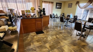 A hotel dining area with a buffet setup, a coffee station, and a seating area with tables and chairs.
