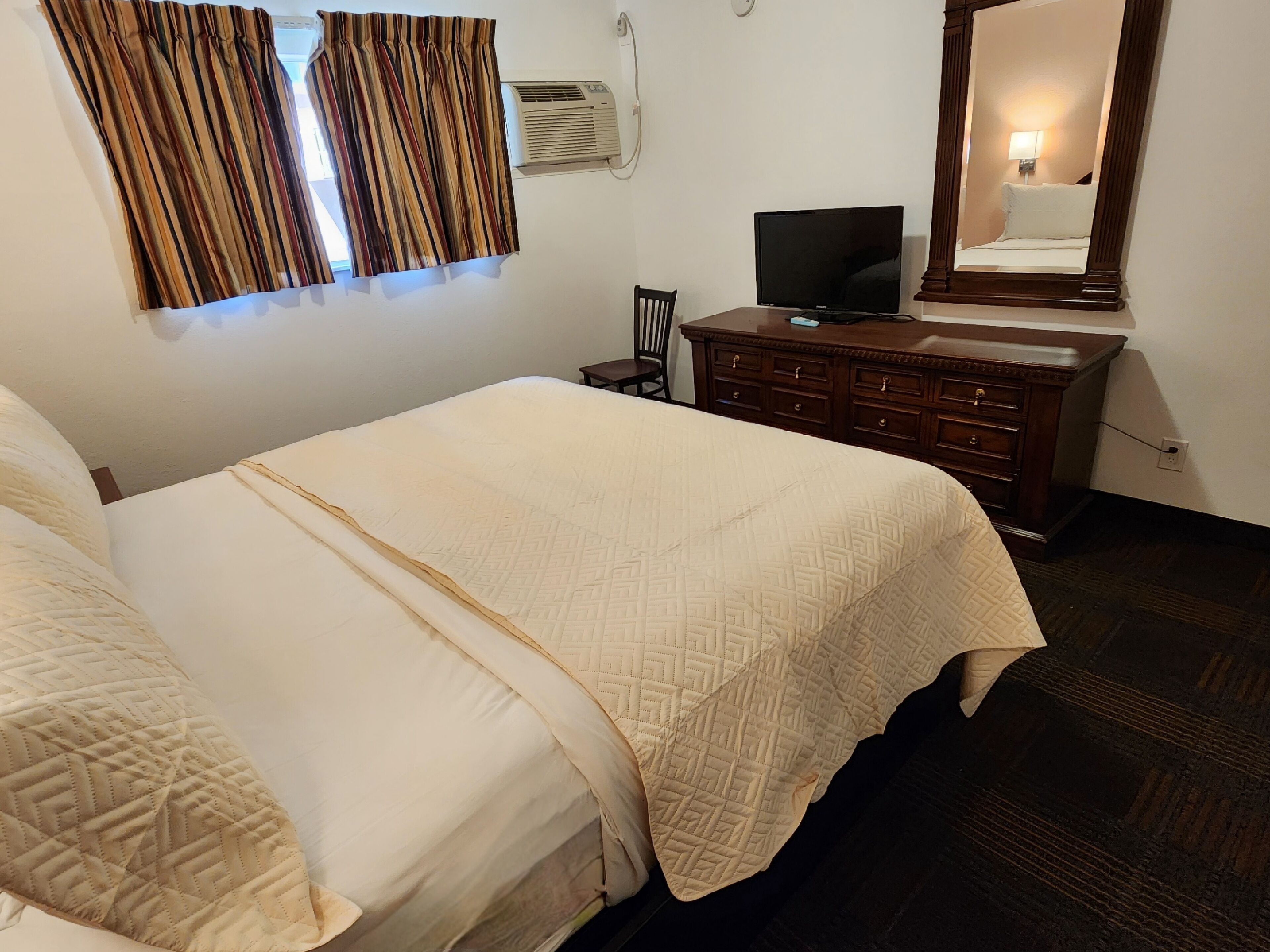 A hotel room with a large bed, a dresser, a television, and a mirror.