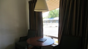 A hotel room with a round table, two chairs, a lamp, and a view of a parking area.