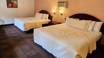 Dos camas individuales con ropa de cama blanca, una mesita de noche pequeña, un aire acondicionado de pared y una obra de arte enmarcada en la pared.