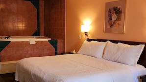 A hotel room with a large bed, a nightstand, a wall-mounted lamp, and a framed picture on the wall.