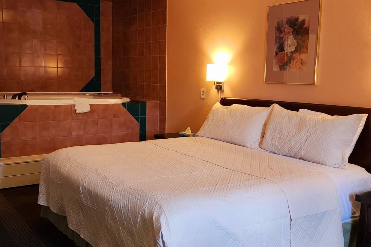Une chambre d’hôtel avec un grand lit, une table de chevet, une lampe fixée au mur et un tableau encadré accroché au mur.
