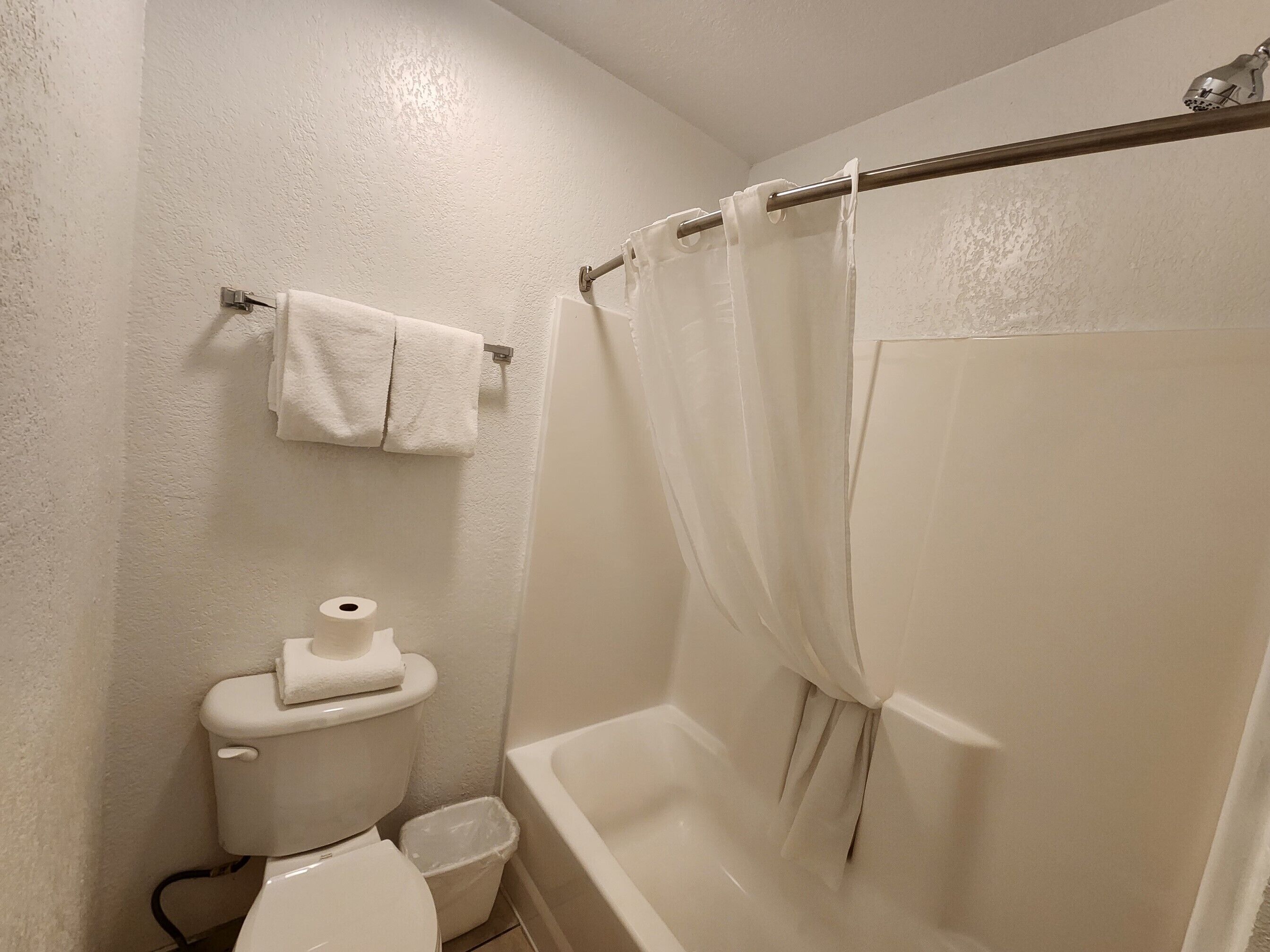 A bathroom with a toilet, a trash bin, and a bathtub with a shower curtain.