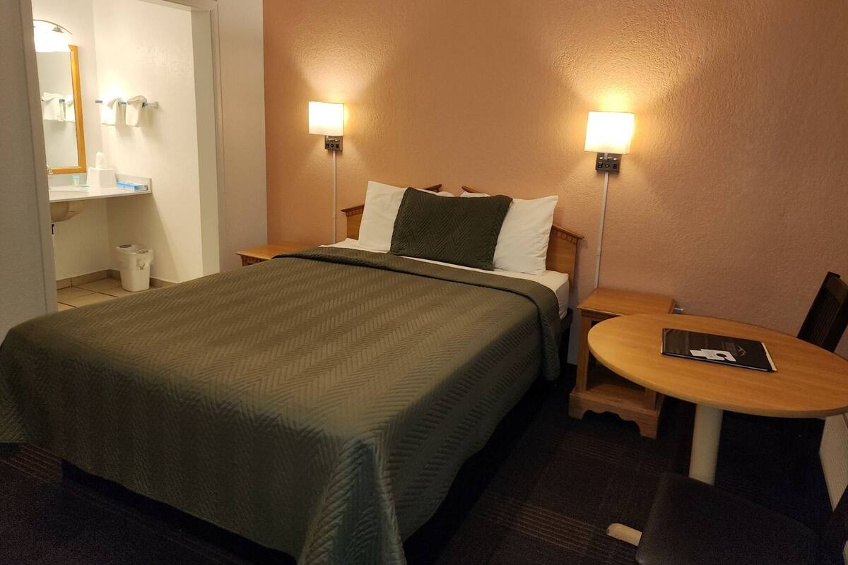 Une chambre d’hôtel avec un lit, des lampes de chevet, une petite table et une chaise.
