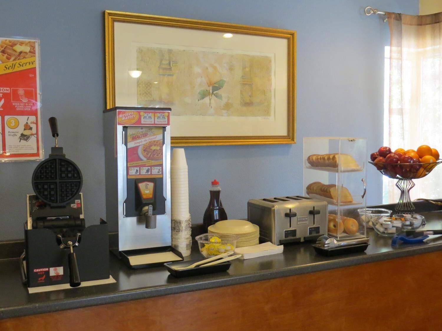 A breakfast bar with a waffle maker, toaster, and a bowl of fruit.