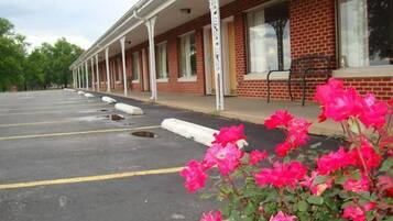 A motel with a row of rooms, a parking lot, and a row of pink flowers in the foreground.
