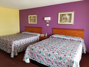 A hotel room with two beds, purple walls, and two framed pictures.