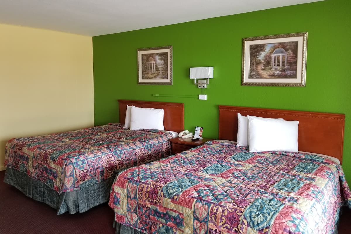A hotel room with two beds, green walls, and framed pictures on the wall.