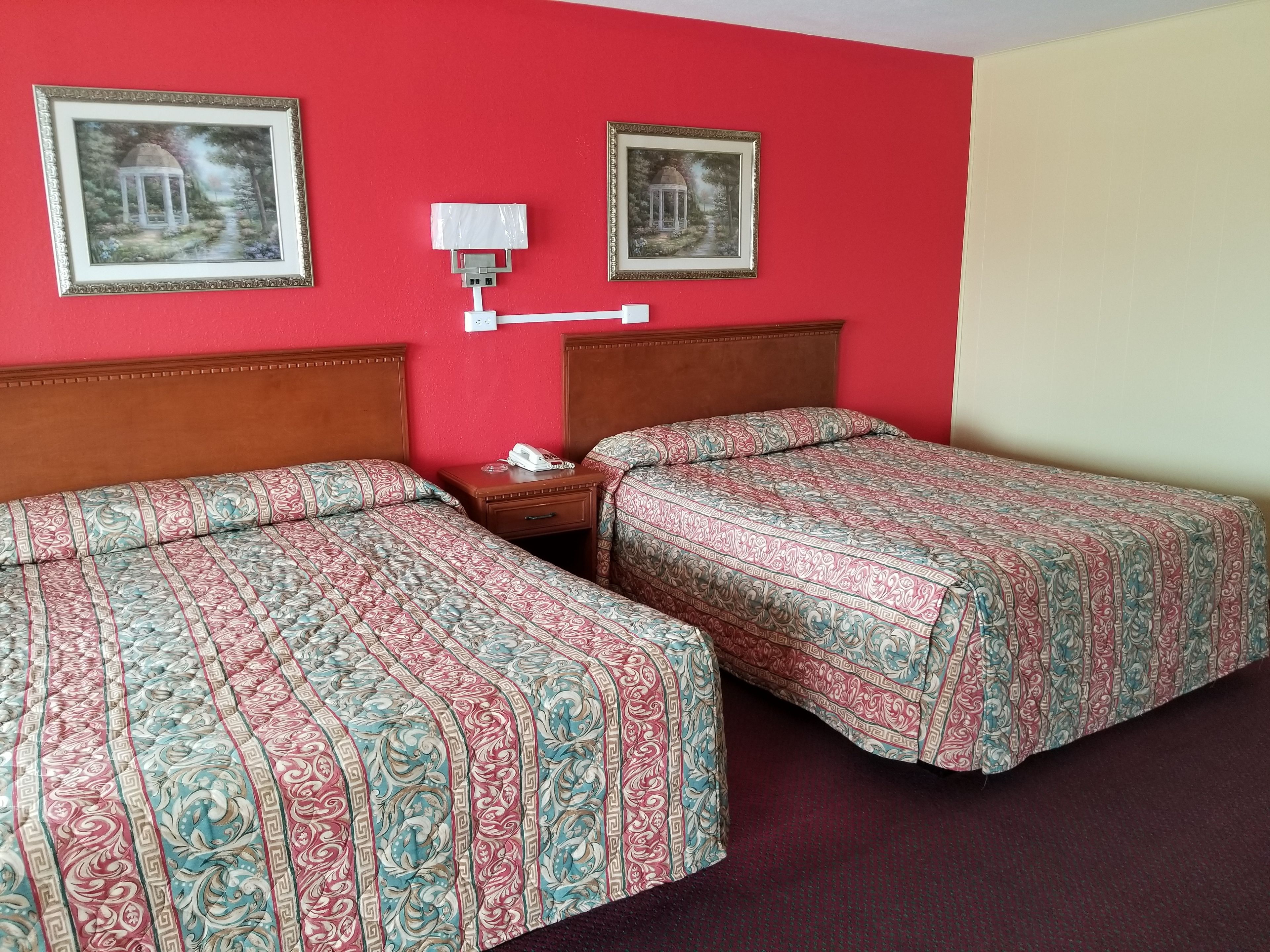 Habitación de hotel con dos camas, una mesita de noche con teléfono y dos cuadros en la pared.
