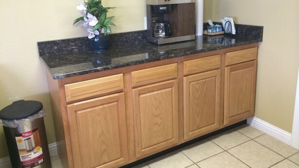 A kitchen with a granite countertop, wooden cabinets, a coffee maker, and a trash can.