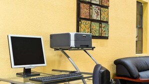 A home office setup with a desktop computer, monitor, keyboard, and printer on a glass desk against a yellow wall. - OYO Hotel Richburg SC I-77 (Richburg)