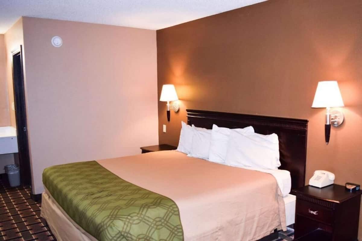 Habitación de hotel con cama, dos lámparas de noche, mesita con teléfono y puerta al baño.
