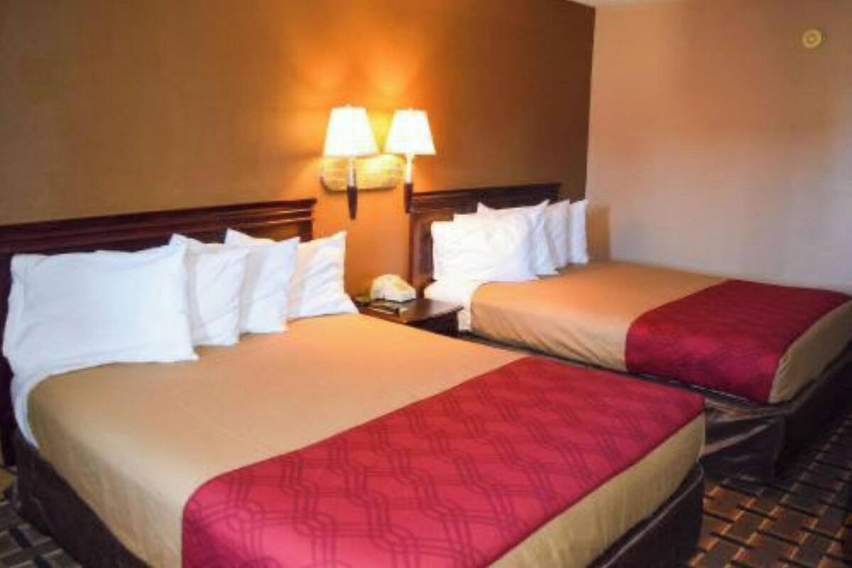 Habitación de hotel con dos camas, cada una con ropa de cama blanca y un detalle rojo. Hay dos lámparas fijadas a la pared entre las camas.