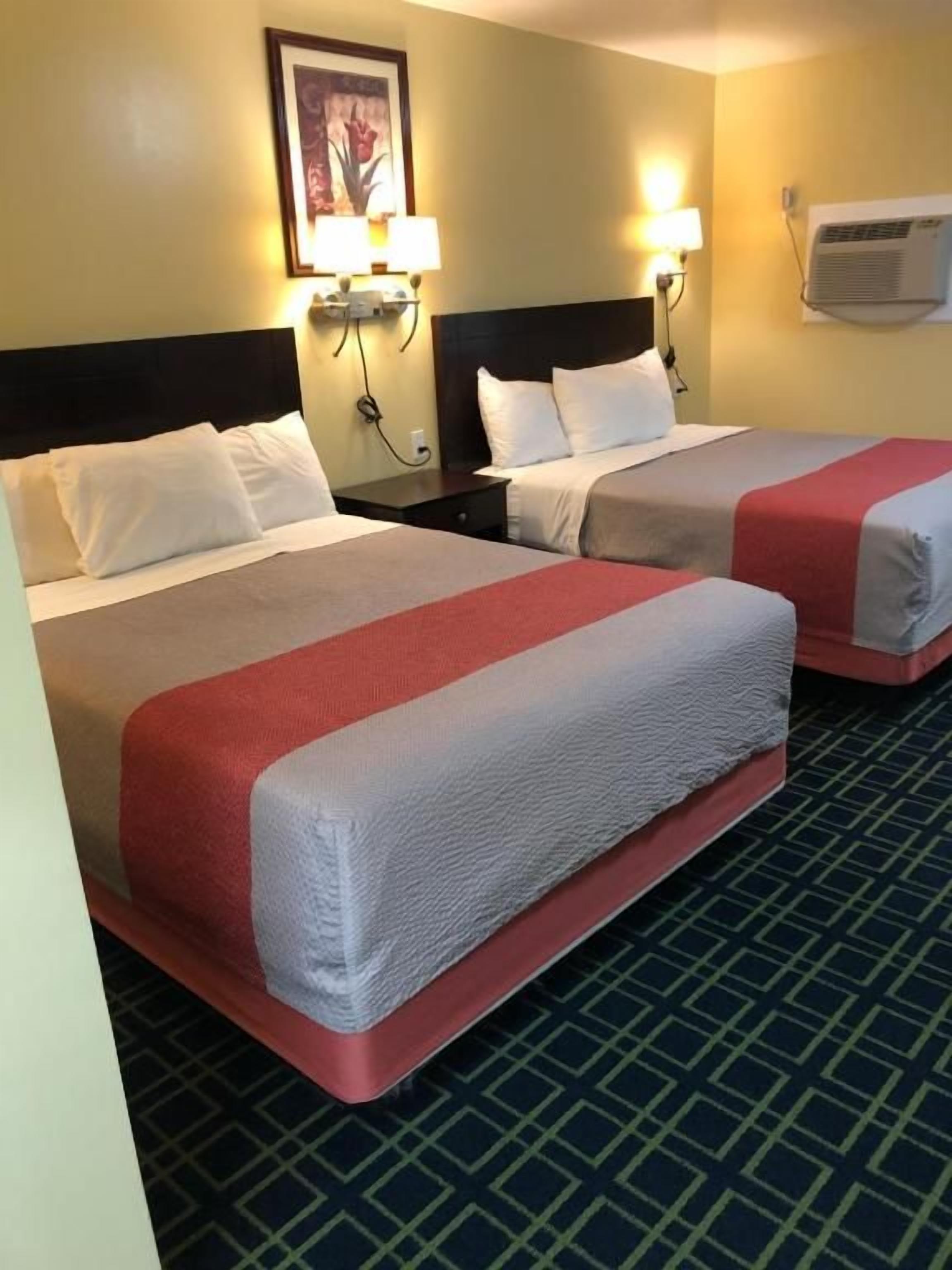 A hotel room with two beds, each with a red and white bedspread, a headboard, and a wall-mounted lamp.