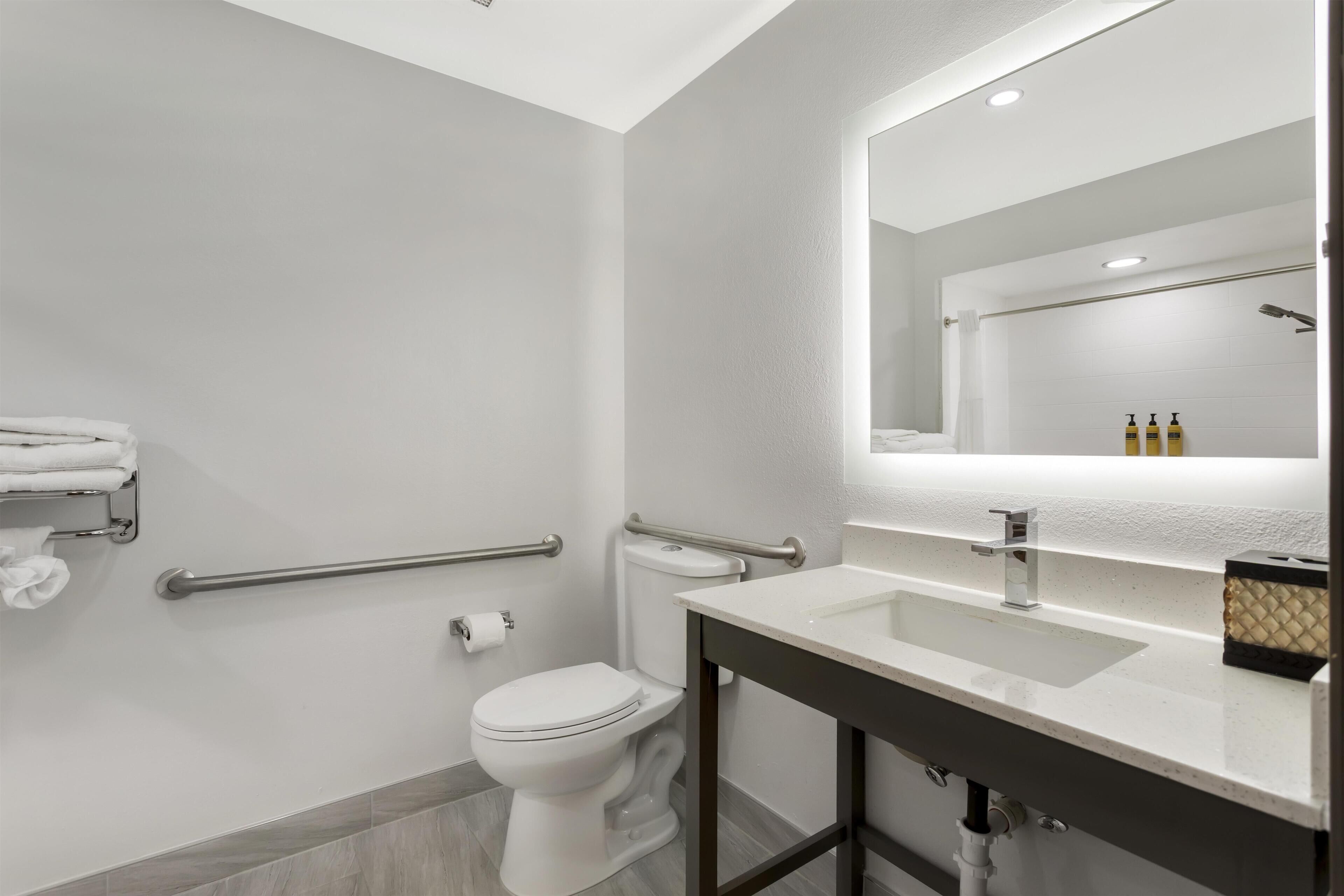 A modern bathroom with a white toilet, a sink with a mirror above it, and a towel rack with towels.
