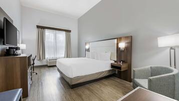 Una habitación de hotel con una cama grande, un escritorio con silla, un televisor y una lámpara.