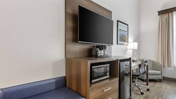 Habitación de hotel con televisión de pantalla plana montada en un mueble de madera, microondas, escritorio con silla y sofá.
