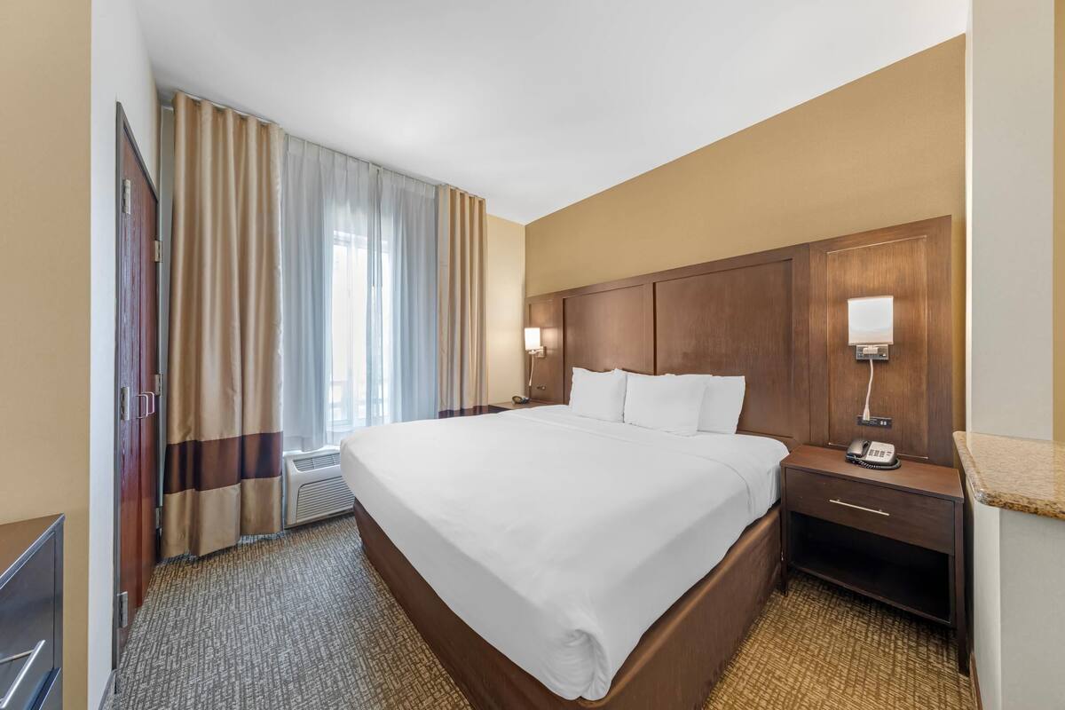 Une chambre d’hôtel avec un grand lit, une table de chevet avec une lampe, une armoire et un téléviseur.