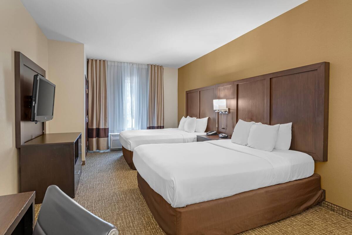 Une chambre d’hôtel avec deux lits, un bureau, une télévision et une fenêtre avec des rideaux.