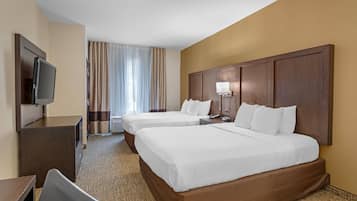 A hotel room with two beds, a desk, a television, and a window with curtains.