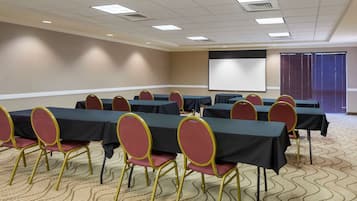 A conference room with tables and chairs, a projector screen, and a carpeted floor.