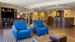 Un hall con sillones azules, mostrador de recepción y una pantalla de televisión.