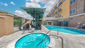 Zona de piscina con dos piscinas, un área de estar cubierta y un edificio con varios balcones.