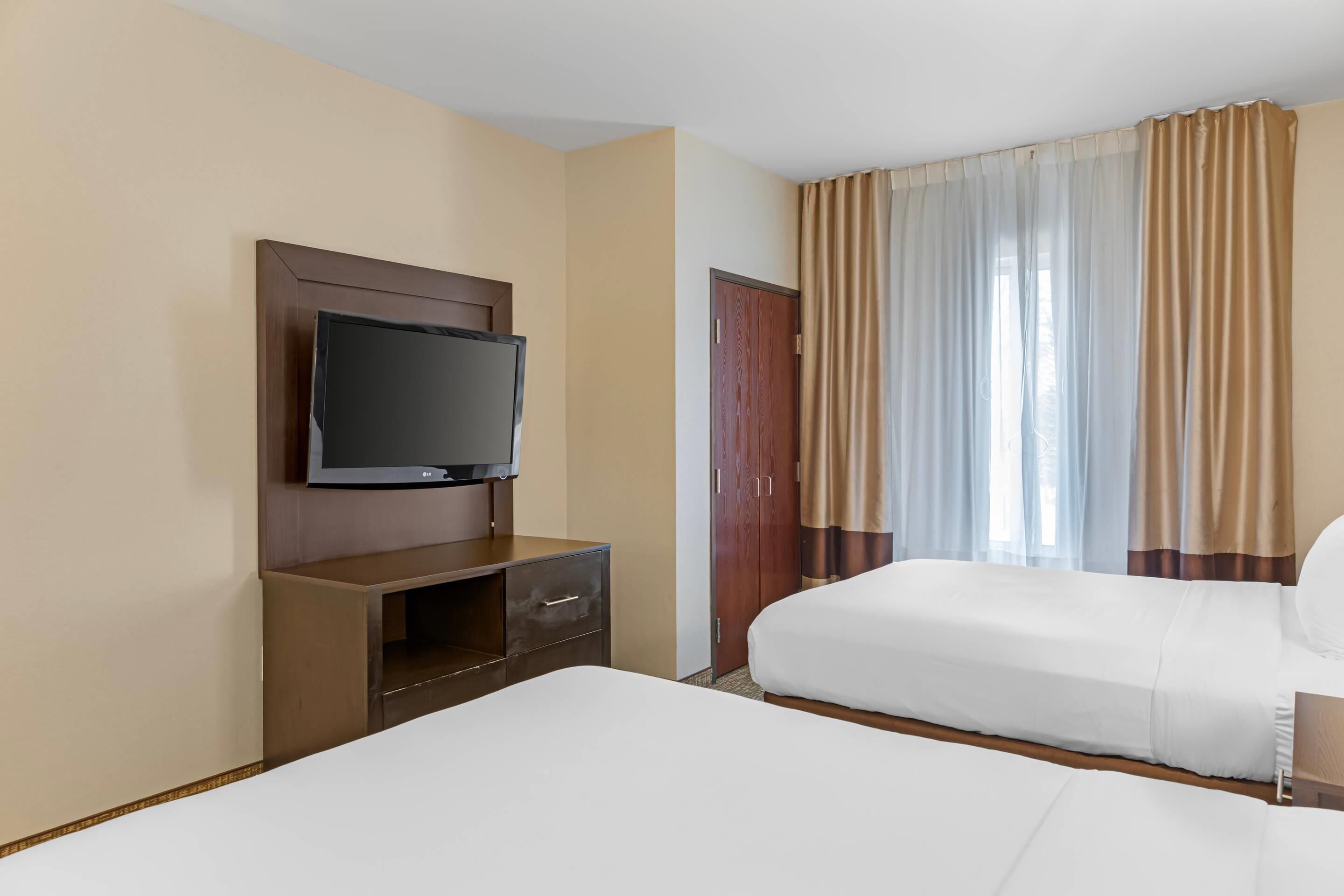 A hotel room with a bed, a TV mounted on a wooden cabinet, and a window with curtains.