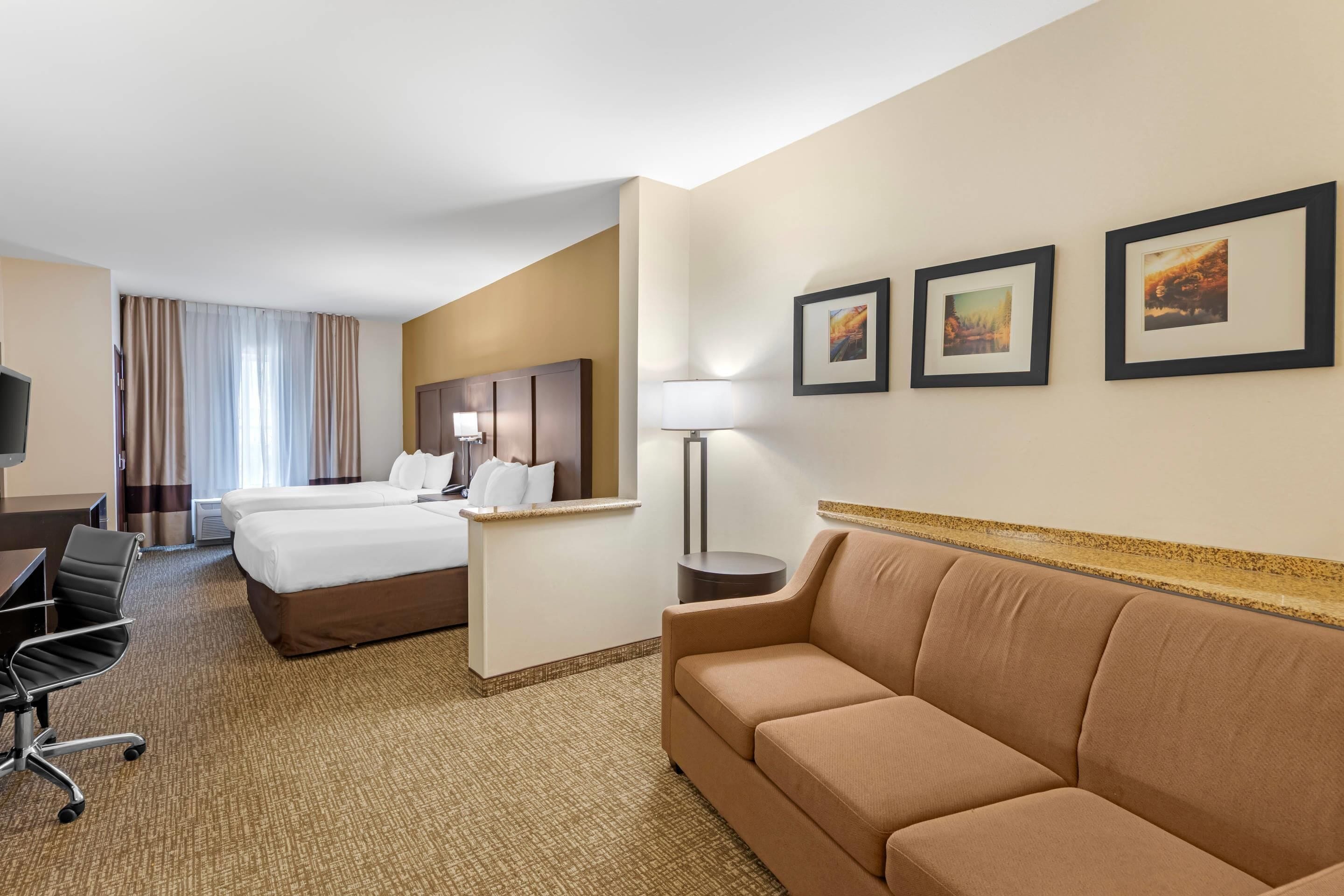 A hotel room with two beds, a desk, a chair, a sofa, and framed pictures on the wall.