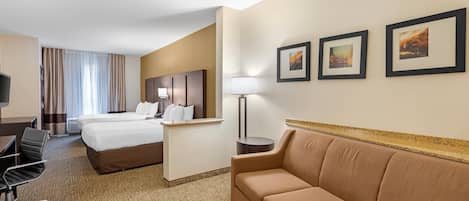 A hotel room with two beds, a desk, a chair, a sofa, and framed pictures on the wall.