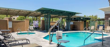 A pool area with a covered seating area, lounge chairs, and a lifeguard stand.