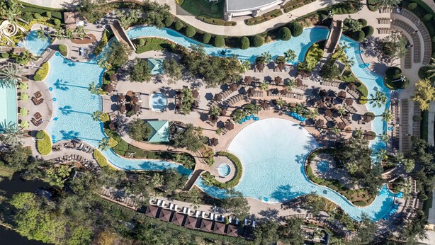 Vista aérea de un complejo turístico con múltiples piscinas, zonas de descanso y palmeras.