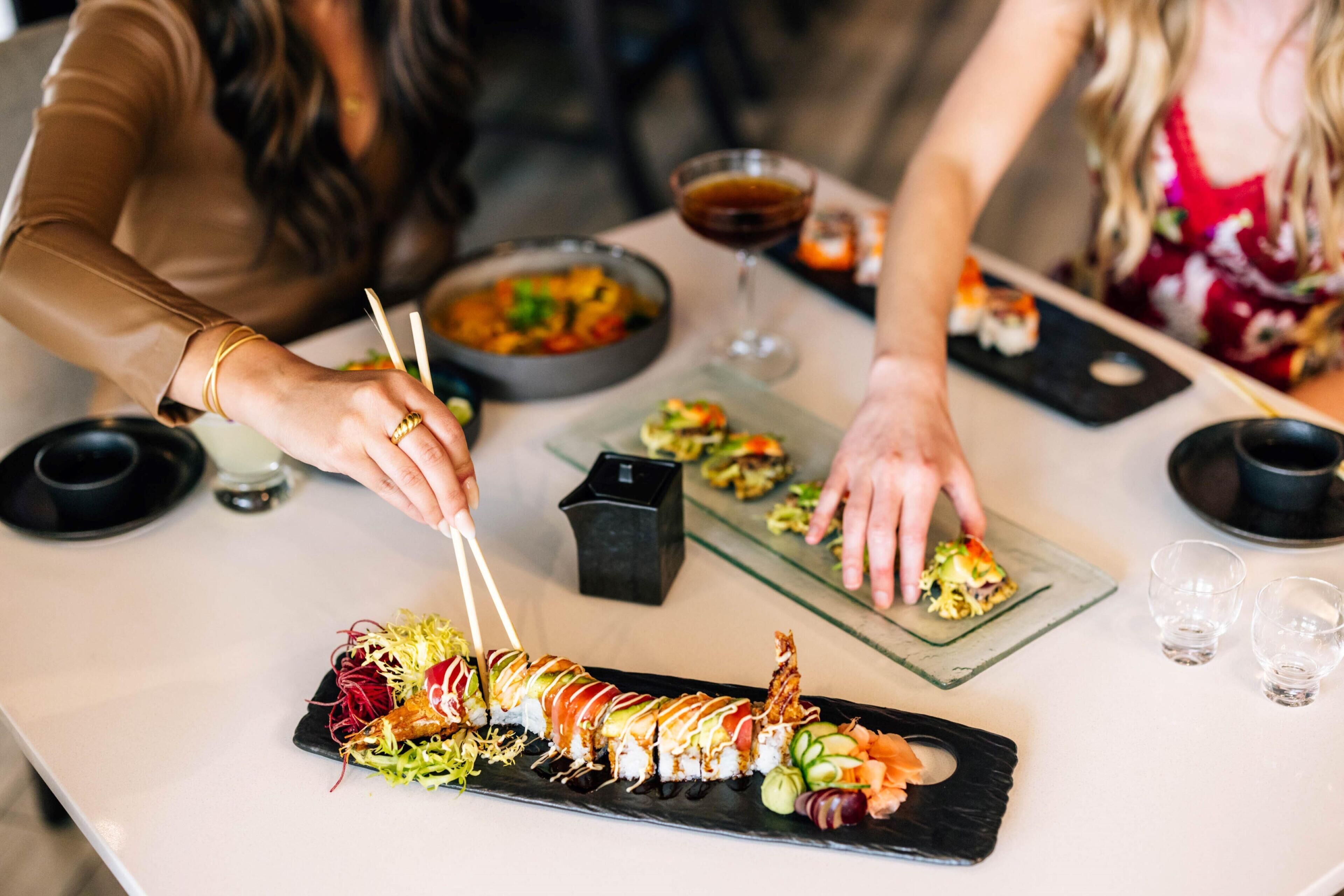 A sushi platter on a table with chopsticks and a glass of drink.