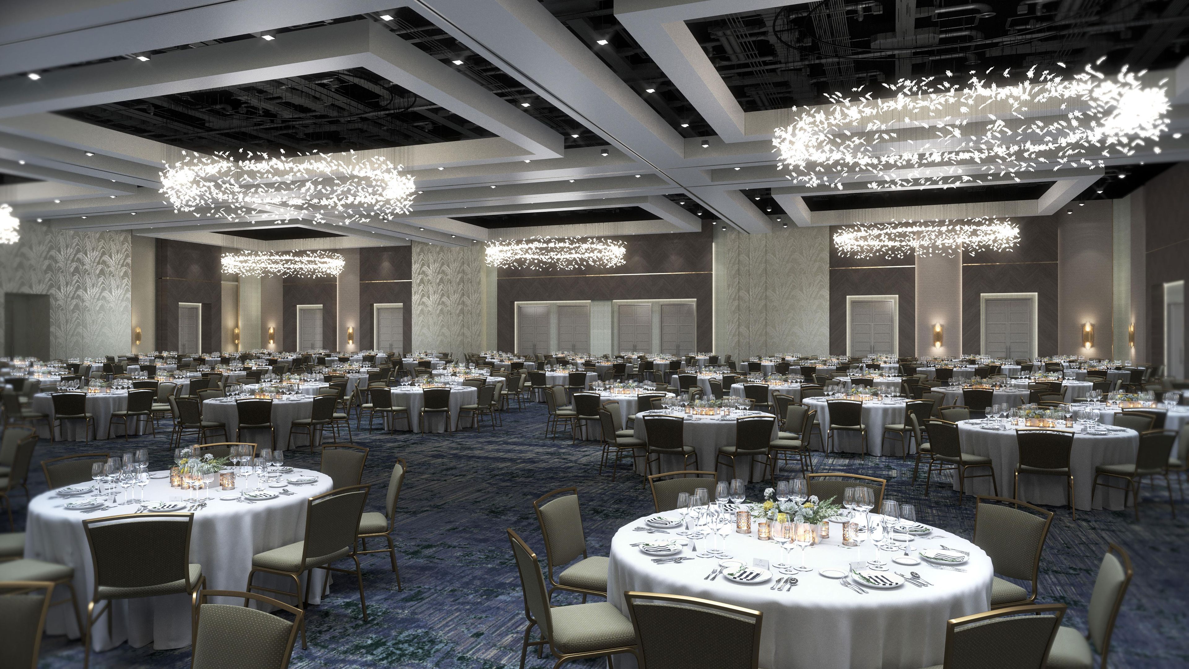 A large banquet hall with round tables, chandeliers, and a carpeted floor.
