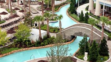 A resort with a pool, lounge chairs, palm trees, and a stone bridge.