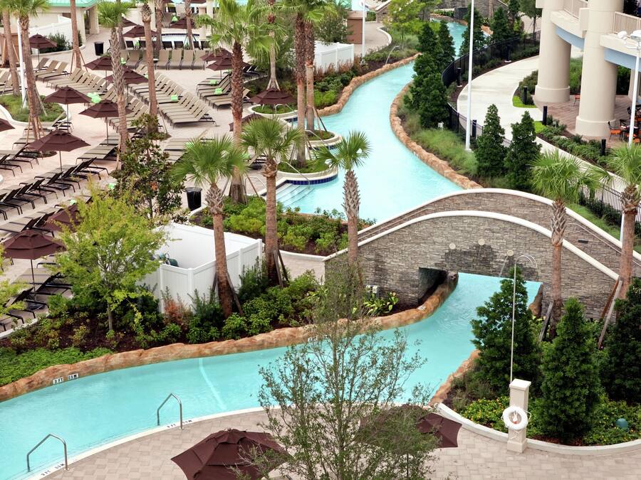 A resort with a pool, lounge chairs, palm trees, and a stone bridge.