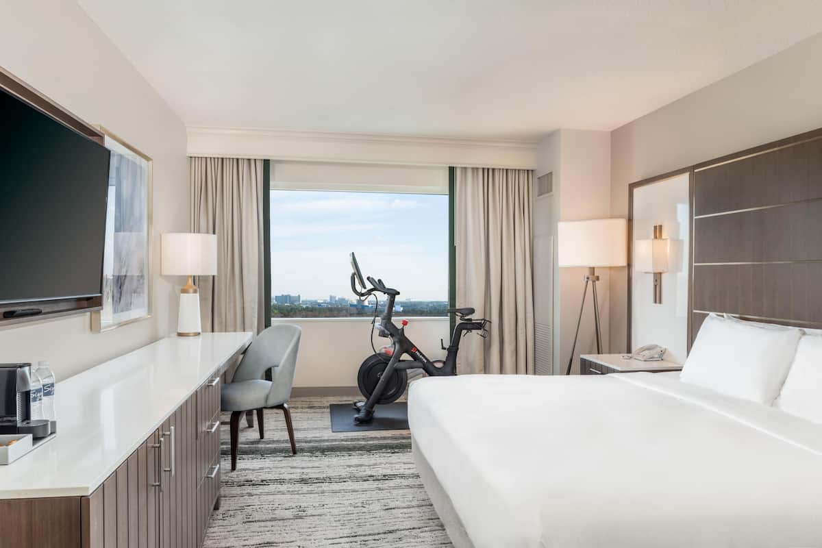 Ein Hotelzimmer mit Bett, Schreibtisch, Stuhl, Fernseher, Fahrrad und Blick auf die Stadt.