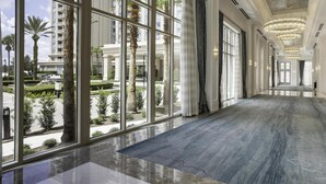 Un pasillo de hotel con amplios ventanales, piso pulido y elegantes candelabros.