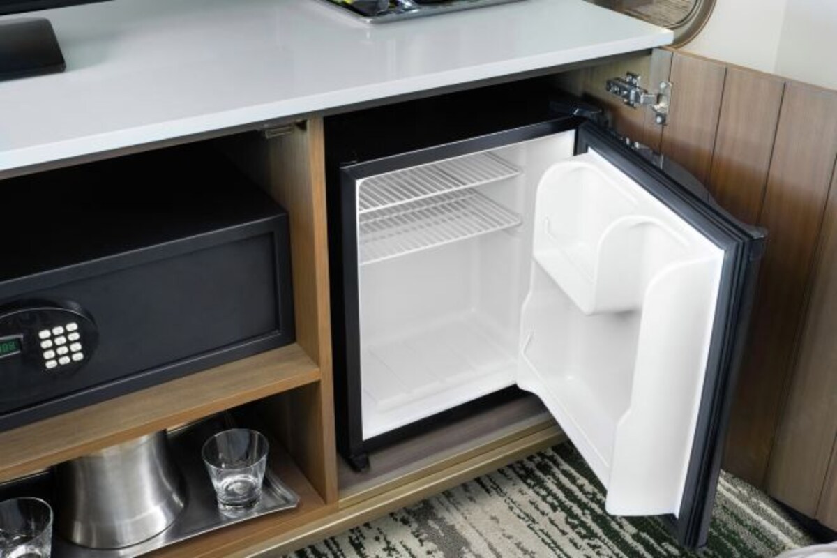 A compact refrigerator with a digital control panel, a small shelf, and a glass on the lower shelf.