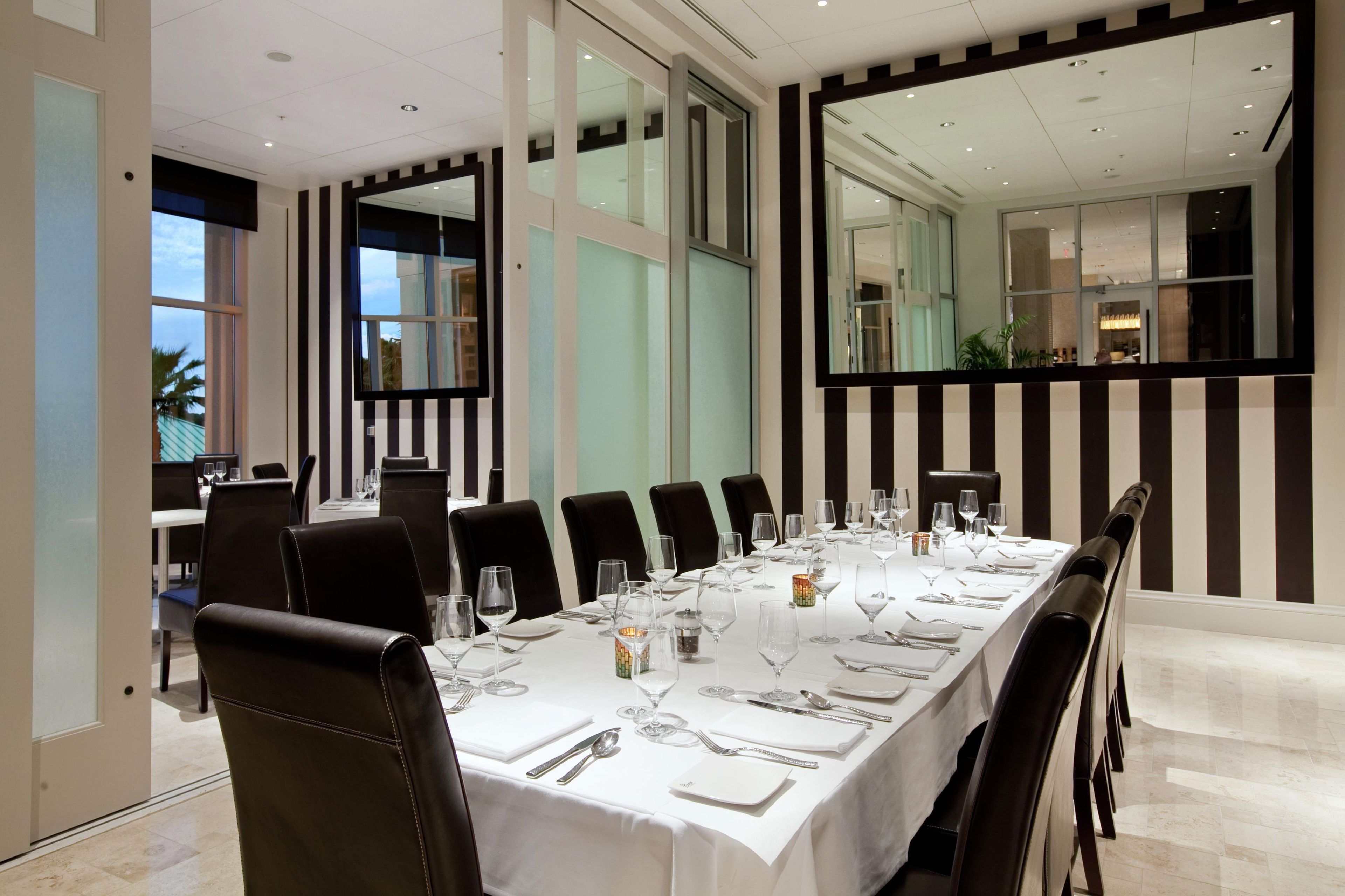 Un comedor con una larga mesa dispuesta para una comida, rodeada de sillas y ventanas amplias con vistas.