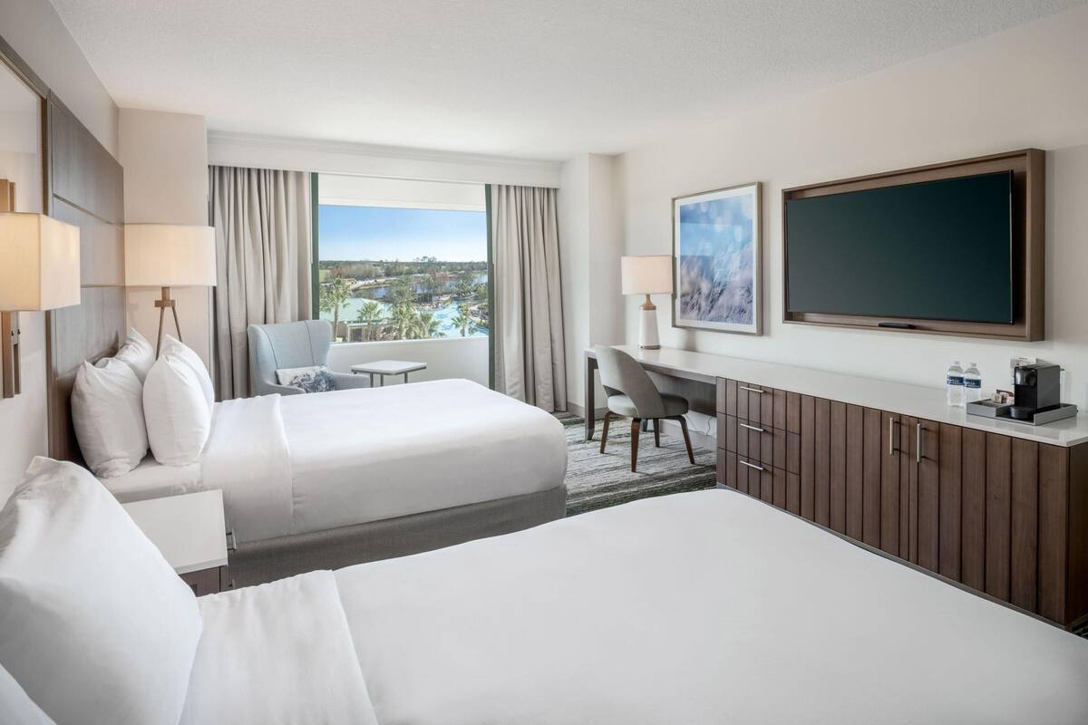 Een hotelkamer met twee bedden, een bureau, een televisie en uitzicht op een resort.