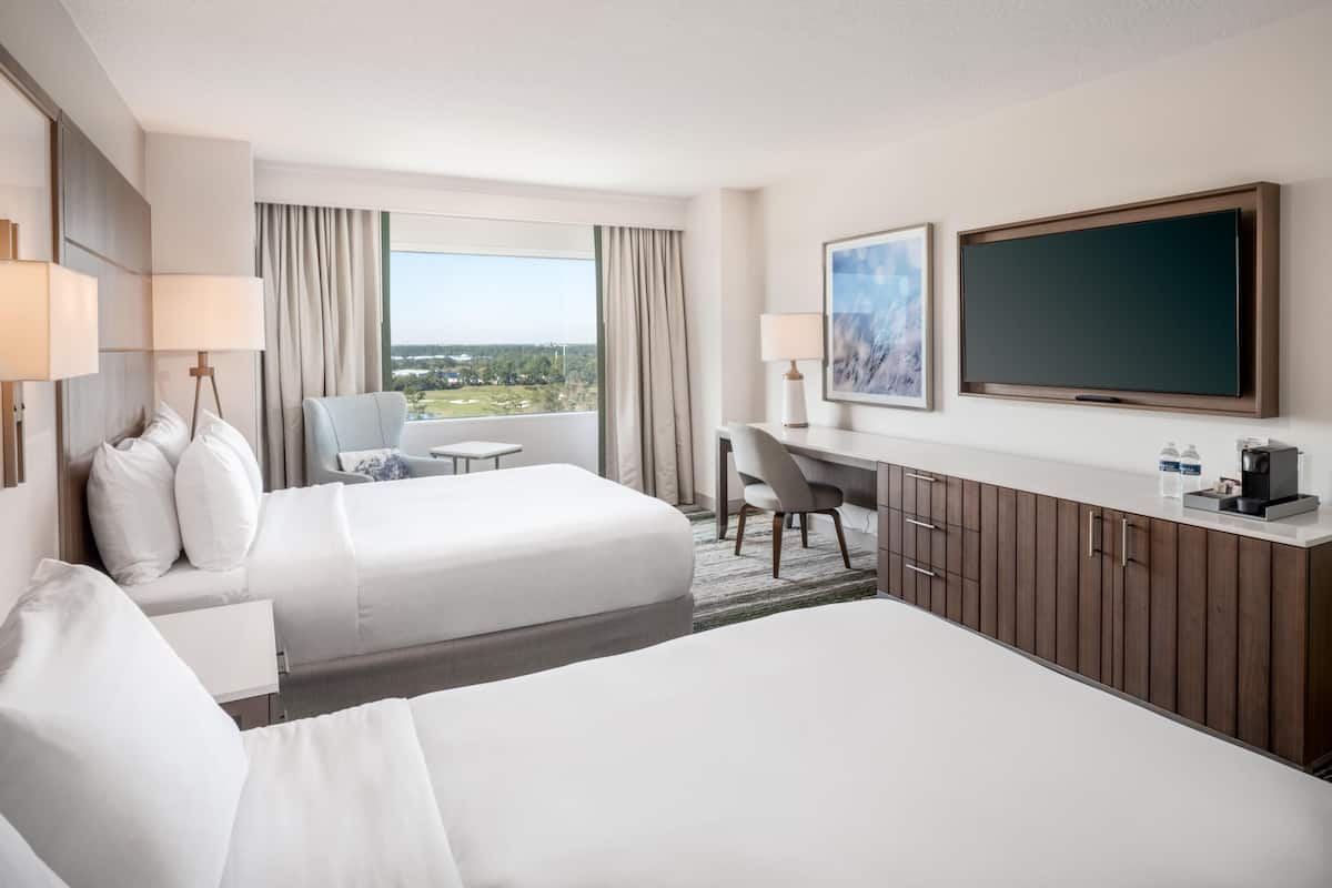 Ein Hotelzimmer mit zwei Betten, einem Schreibtisch, einem Sessel, einem Fernseher und einem Fenster mit Blick.