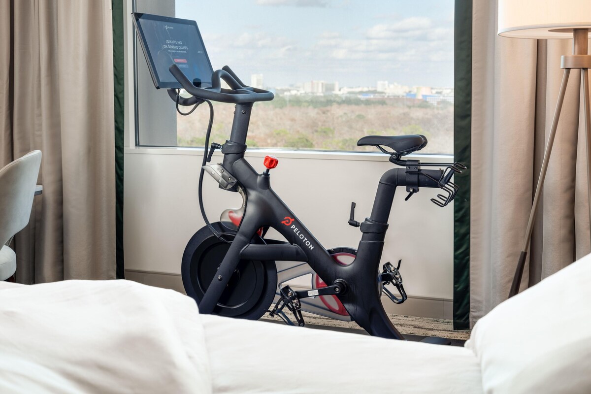 An electric bike with a screen attached, positioned in a room with a large window offering a city view.